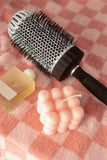 The Jumbo Round brush with dome top laying next to a hair serum bottle and pink bubble candle.