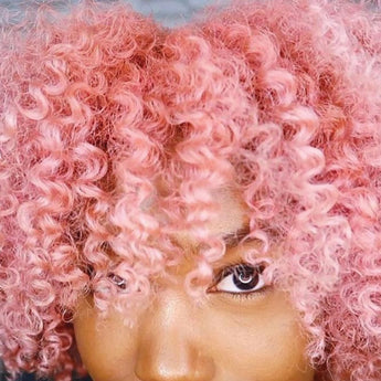 Closeup of eyes and bangs of young lady with thick, pink kinky-curly hair.