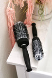Large and Small Ionic Thermal Round brushes on bathroom vanity next to pink houseplant.