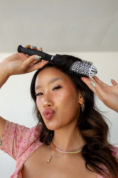 Young woman making a kissy face while styling her bangs with the small ionic thermal round brush.