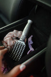 An upside down Tangle Buster Styler Tiny in a car's center console next to scrunchies and a barrette.