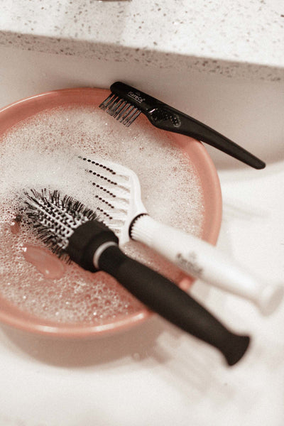 A freshly cleaned Small Ionic thermal round brush soaking in soapy water with a detangling brush and the Kareco brush brush.
